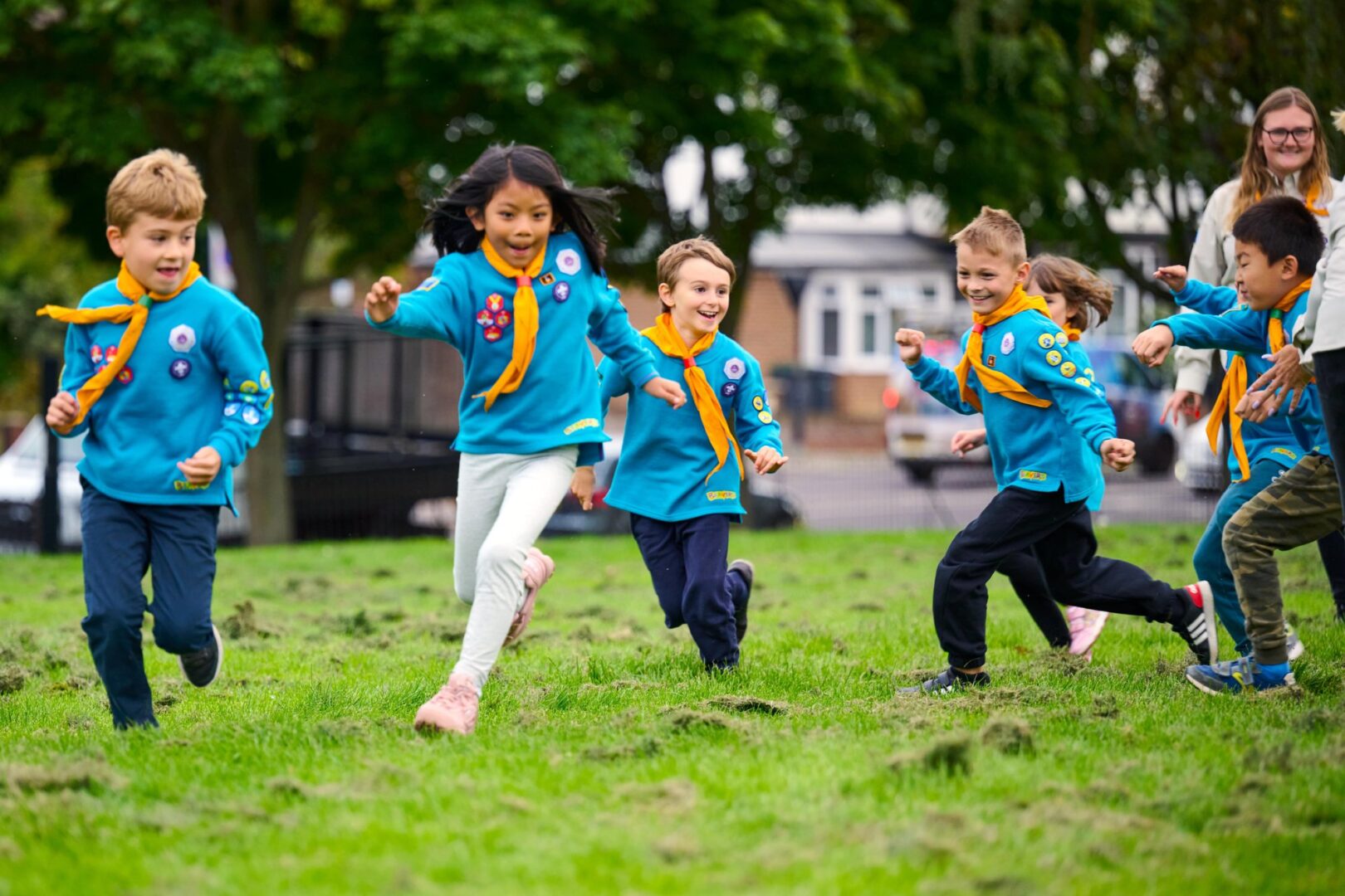 Beavers in turquoise jumpers and yellow neckers running across a grassy field during a game