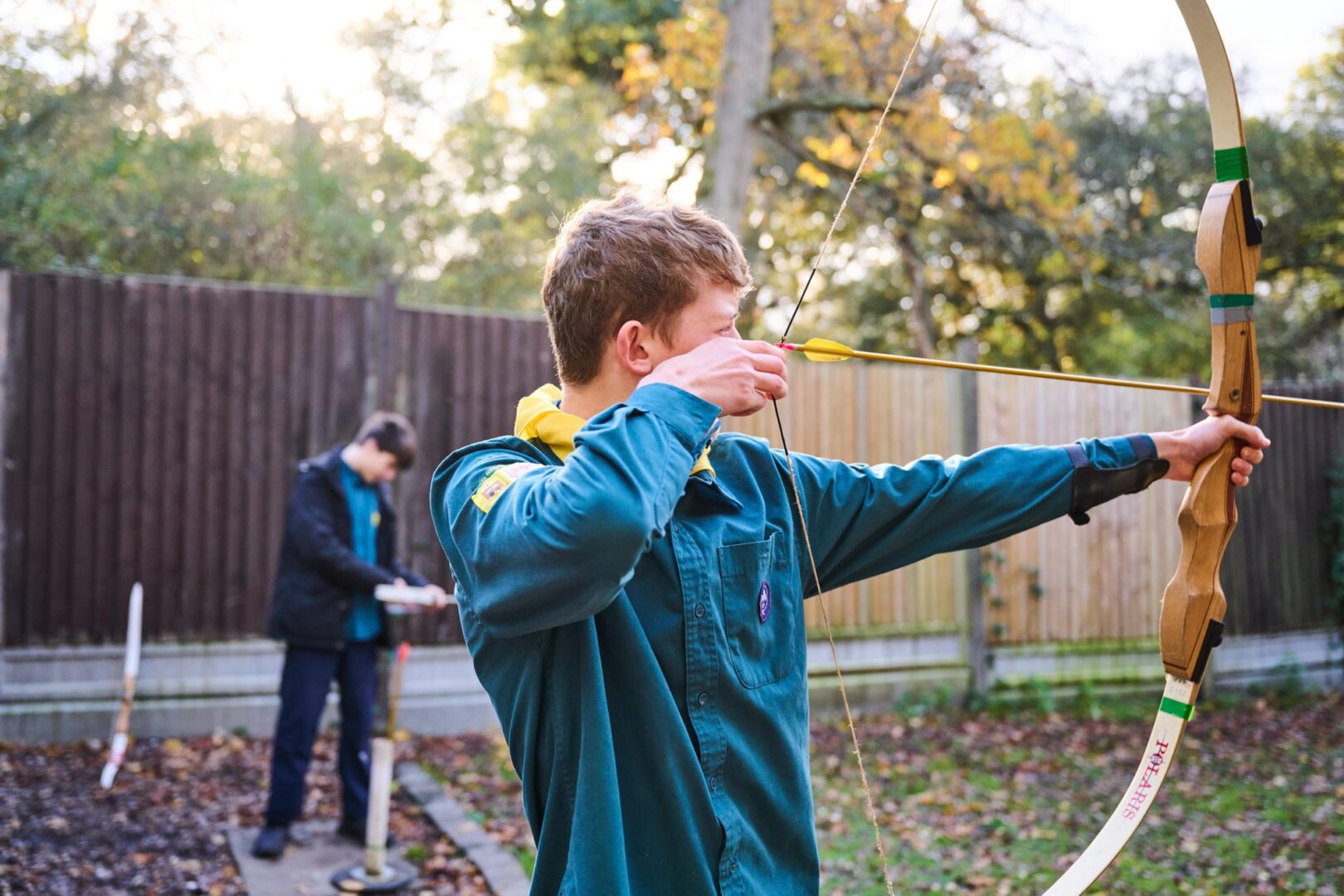 A Scout in uniform drawing a bow during outdoor archery