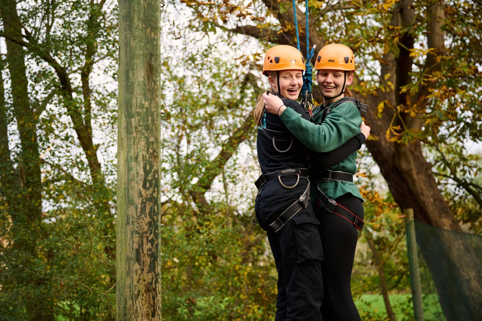 Two young people in climbing helmets and harnesses hugging and smiling during crate stacking