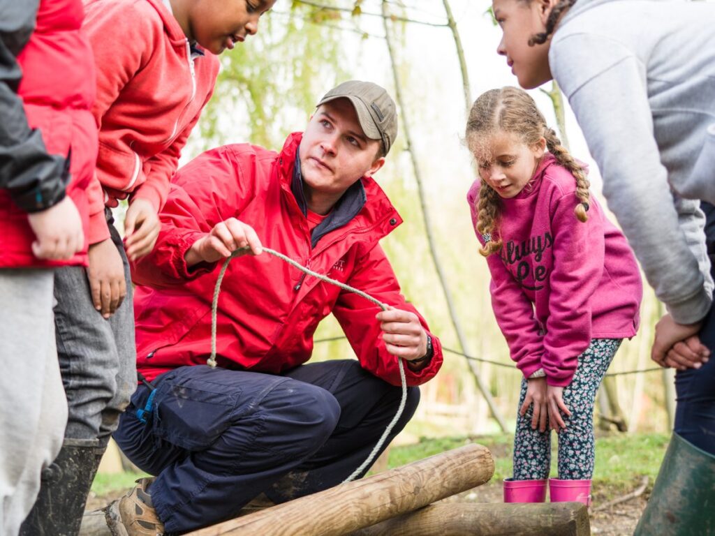Scout volunteer teaching rope skills to young people outdoors